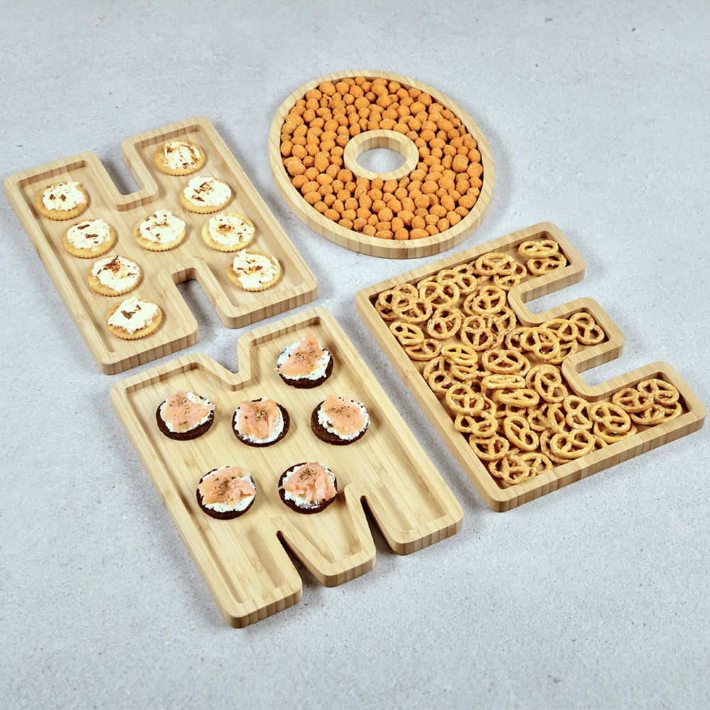 Servierbretter aus Bambus in Form der Buchstaben H, O, M, E, gefüllt mit verschiedenen Snacks, aus der Vogelperspektive.