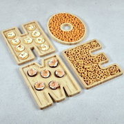 Servierbretter aus Bambus in Form der Buchstaben H, O, M, E, gefüllt mit verschiedenen Snacks, aus der Vogelperspektive.