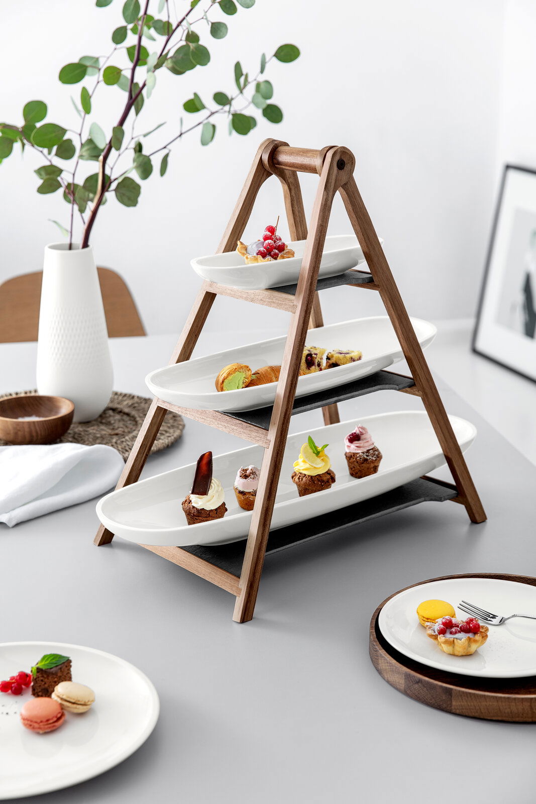 Villeroy & Boch Eye Catcherset 4-tlg. ARTESANO ORIGINAL Dreistöckige Etagere aus Holz mit weißen Porzellantellern, dekoriert mit verschiedenen kleinen Desserts, seitliche Perspektive.