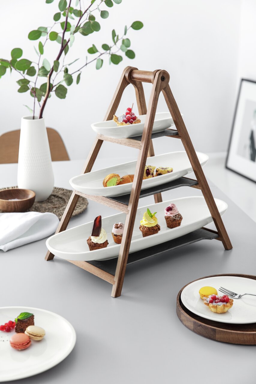 Houten etagère met drie verdiepingen, met witte porseleinen borden, versierd met diverse kleine dessertjes, zijaanzicht.