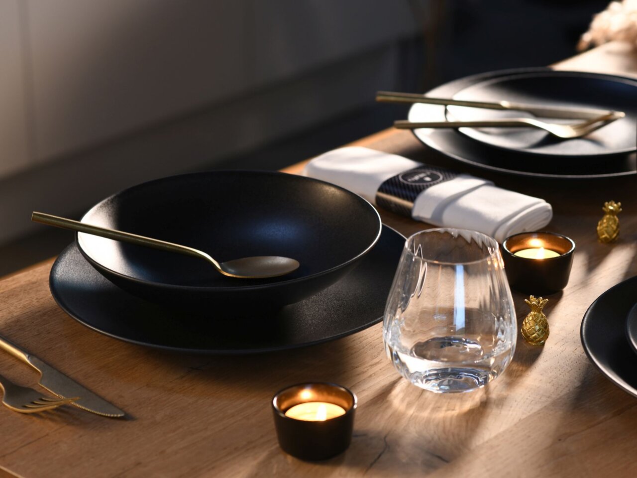 Elegantes Tafelservice Soft Touch 12-tlg in Schwarz mit goldenen Besteck, Glas und Kerzen auf einem Holztisch, seitliche Perspektive