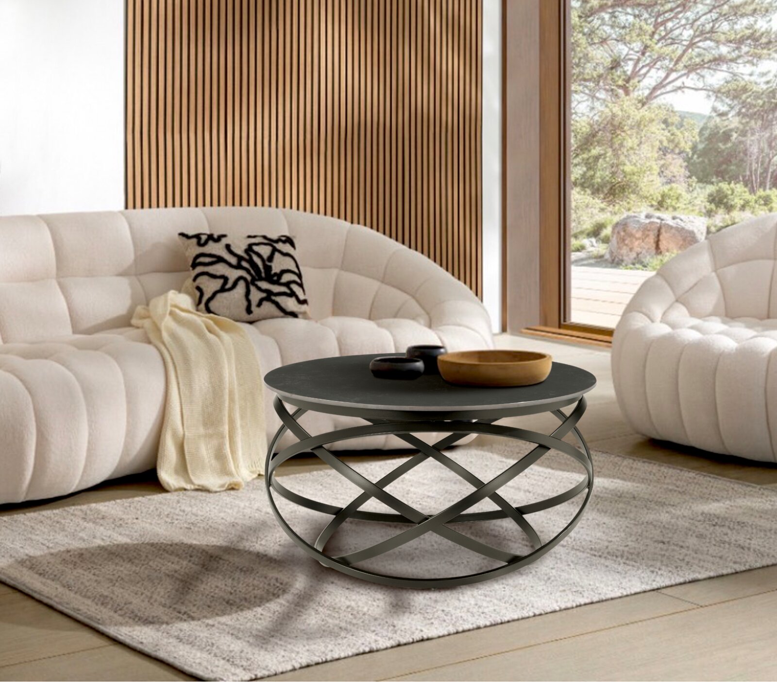 Moderner Couchtisch mit schwarzer runder Tischplatte und kunstvollem Metallgestell, frontal im Wohnzimmer mit weißen Sofas und Holzwand.