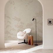 Beige Tapete mit dezentem botanischem Blattmuster im modernen Wohnzimmer-Setting, frontale Perspektive; davor weißer Sessel, schwarzer Stehlampe und kleiner Holzhocker.
