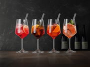 Vier elegante Weingläser mit bunten Cocktails und Eiswürfeln, dekoriert mit Zitrusfrüchten und Kräutern, auf einem Holztisch vor dunklem Hintergrund. Seitliche Perspektive.