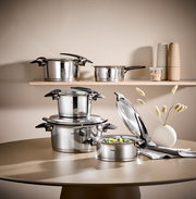 Topfset Intensa 5-tlg. aus Edelstahl, bestehend aus mehreren Töpfen mit Deckeln, auf einem Tisch und einem Regal präsentiert. Perspektive: seitlich.