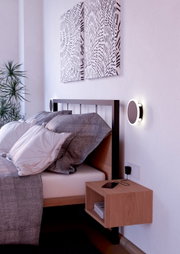 Moderne Wandleuchte TALAMELLO 1 neben einem Bett, seitliche Perspektive