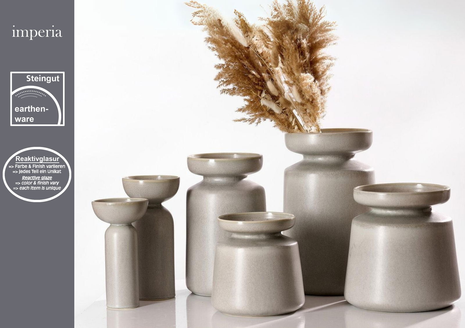 Sechs graue Vasen der Serie Imperia aus Steingut mit Reaktivglasur, in verschiedenen Größen, von vorne betrachtet. Eine Vase ist mit getrockneten Gräsern dekoriert.