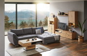 Gemütliche Wohnzimmer-Ecke mit grauem Ecksofa und Holzmöbeln, Blick auf Berge und See durch große Fenster.