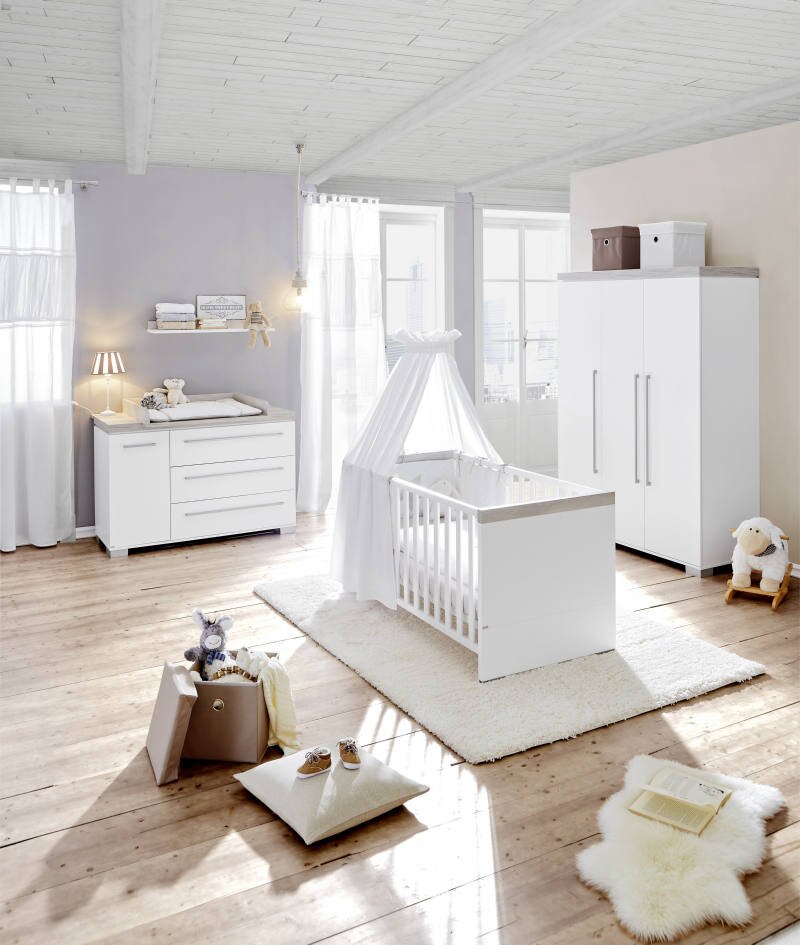 Helles und modernes Babyzimmer mit Kinderbett, Wickelkommode und Kleiderschrank in weißer Farbe, aus der Perspektive eines diagonalen Blicks auf den Raum.