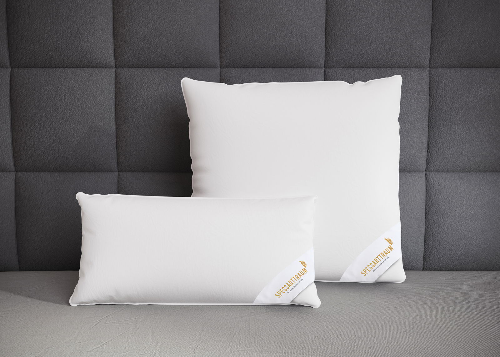 Zwei weiße Spessarttraum 3-Kammerkissen auf einem grauen Bett, frontal fotografiert vor einer gepolsterten Wand.