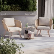 Zwei Loungesessel mit beigen Kissen und einem kleinen runden Tisch in einem modernen Außenbereich, seitliche Perspektive.