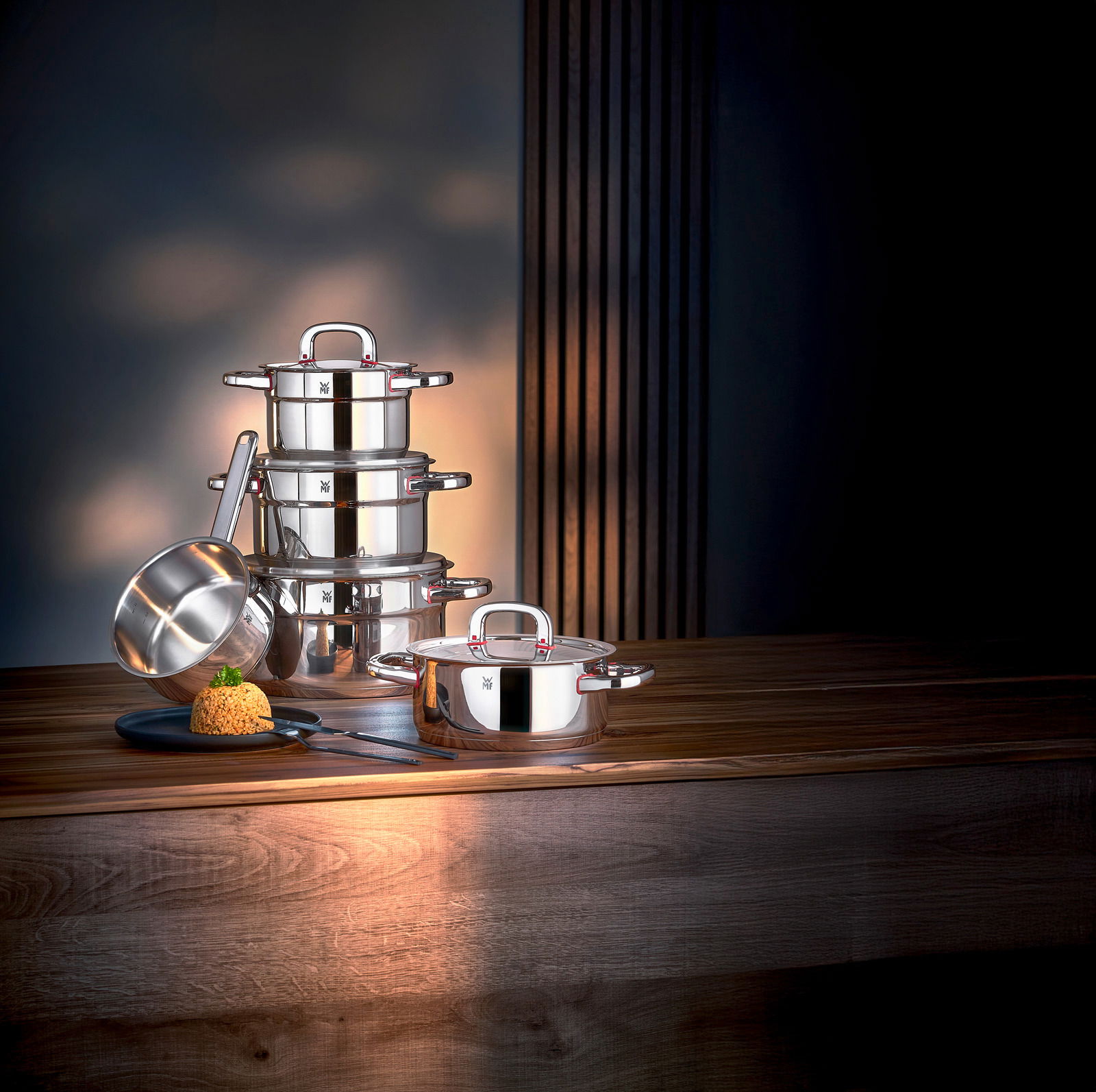 Elegantes 3-teiliges Topfset aus Edelstahl, bestehend aus gestapelten Töpfen und einer Stielkasserolle, auf einem Holztisch in seitlicher Perspektive präsentiert.