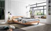 Modern houten bedframe met zwevend ontwerp, zijaanzicht in een stijlvolle slaapkamer met grote ramen en decoratieve elementen.