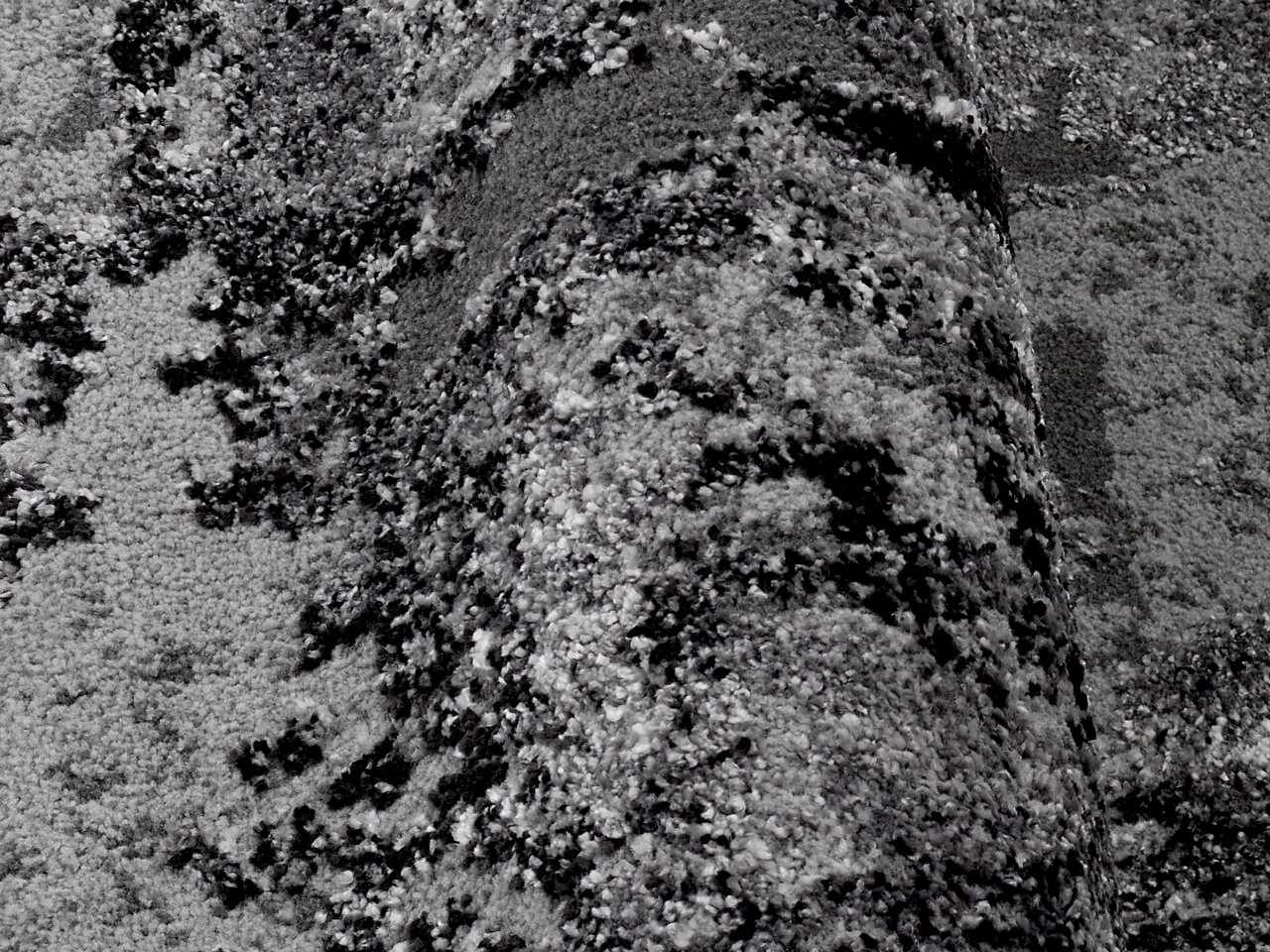 Nahaufnahme eines grauen Teppichs mit abstraktem Muster, perspektivisch von der Seite aufgenommen.