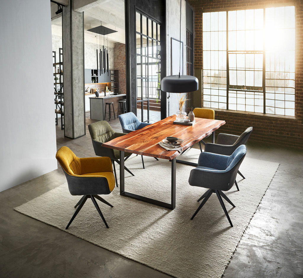Moderner Essbereich mit einem großen Holztisch und verschiedenen Sesseln in einem industriellen Loft mit großen Fenstern. Perspektive von schräg oben.