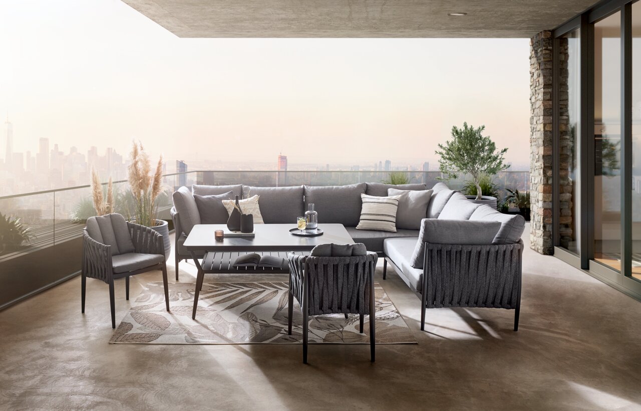 Moderner Gartentisch auf einer stilvollen Terrasse mit Blick auf die Stadt, umgeben von eleganten grauen Sitzmöbeln und Pflanzen, aus der Perspektive von vorne.