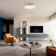 Modernes Wohnzimmer mit runder, flacher LED-Deckenleuchte in Weiß, blauem TV-Lowboard und Vitrine sowie cognacfarbenem Ledersessel; Perspektive: Weitwinkelaufnahme leicht von unten in den Raum.