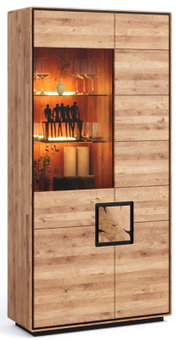 Moderne Vitrine aus hellem Holz mit Glasfach und warmer LED-Innenbeleuchtung, seitlich rechts mit Holztür und schwarzem Griffdetail; Frontansicht in leichter Schrägperspektive von links.