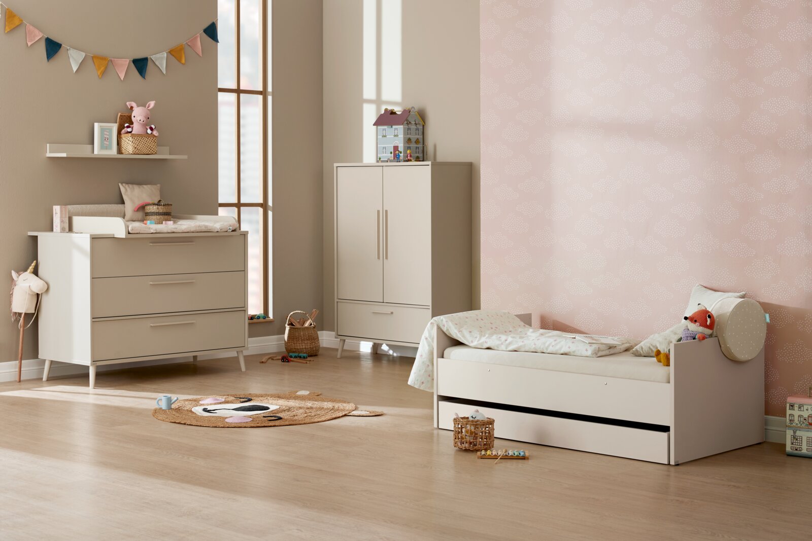 Modernes Kinderzimmer mit cremefarbenem Kinderbett mit Ausziehbett/Schublade, passender Kommode mit Wickelauflage und zweitürigem Schrank; Perspektive: frontale, leicht seitliche Raumansicht.