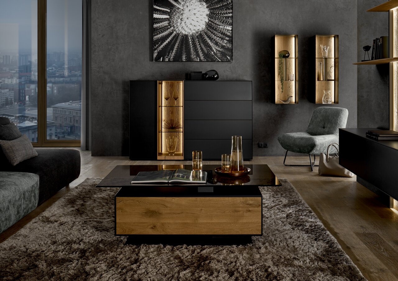 Musterring Couchtisch TREVIO Moderne Wohnzimmeransicht mit Couchtisch aus Holz und Glas, Highboard mit LED-Beleuchtung und stilvollen Dekorationen, seitliche Perspektive.