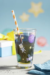 Kinderglas mit Weltraummotiv, Strohhalm und Geschenk im Hintergrund, seitliche Perspektive