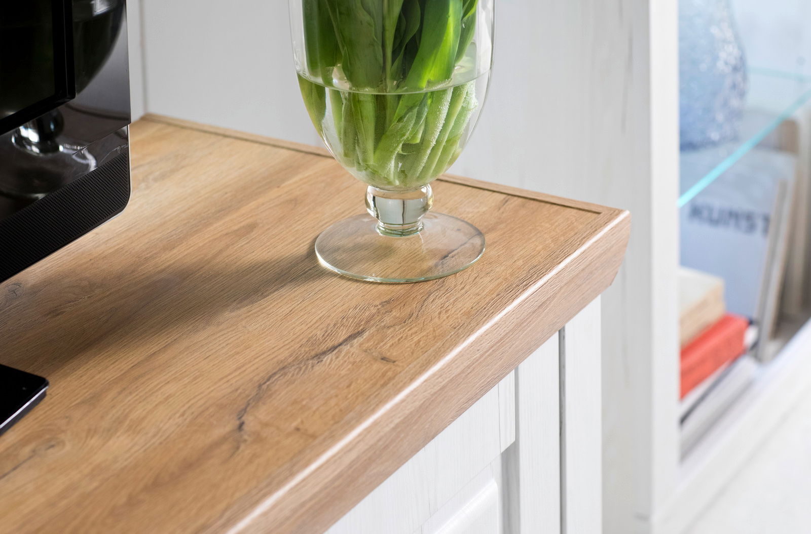 Nahaufnahme einer Holzoberfläche mit einer Glasvase mit grünen Blättern darauf, seitliche Perspektive.