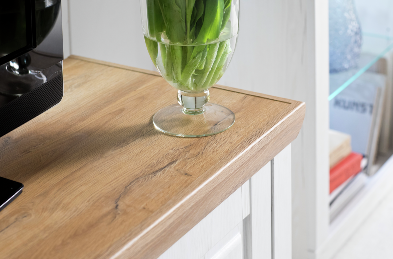 Nahaufnahme einer Holzoberfläche mit einer Glasvase mit grünen Blättern darauf, seitliche Perspektive.