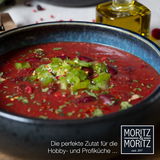 Nahaufnahme eines blauen Suppentellers mit roter Suppe, garniert mit grünen Paprikastücken und Kräutern, seitliche Perspektive.