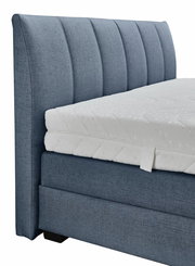 Seitliche Ansicht eines blauen Boxspringbetts mit gepolstertem Kopfteil und weißer Matratze.
