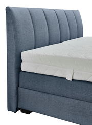 Seitliche Ansicht eines blauen Boxspringbetts mit gepolstertem Kopfteil und weißer Matratze.