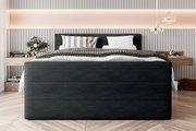Frontale Ansicht eines stilvollen Boxspringbetts mit dunklem Stoffbezug, dekoriert mit Kissen und Decken in einem modernen Schlafzimmer.