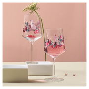 Zwei Weingläser mit tropischem Design, verziert mit Papageien und exotischen Früchten, auf einem Tisch mit rosa Hintergrund. Seitliche Perspektive.