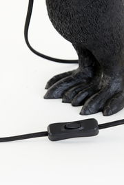 Nahaufnahme der Tischleuchte mit einem schwarzen Kabel und Schalter, sowie einem dekorativen Fuß in Tierform. Perspektive von unten.