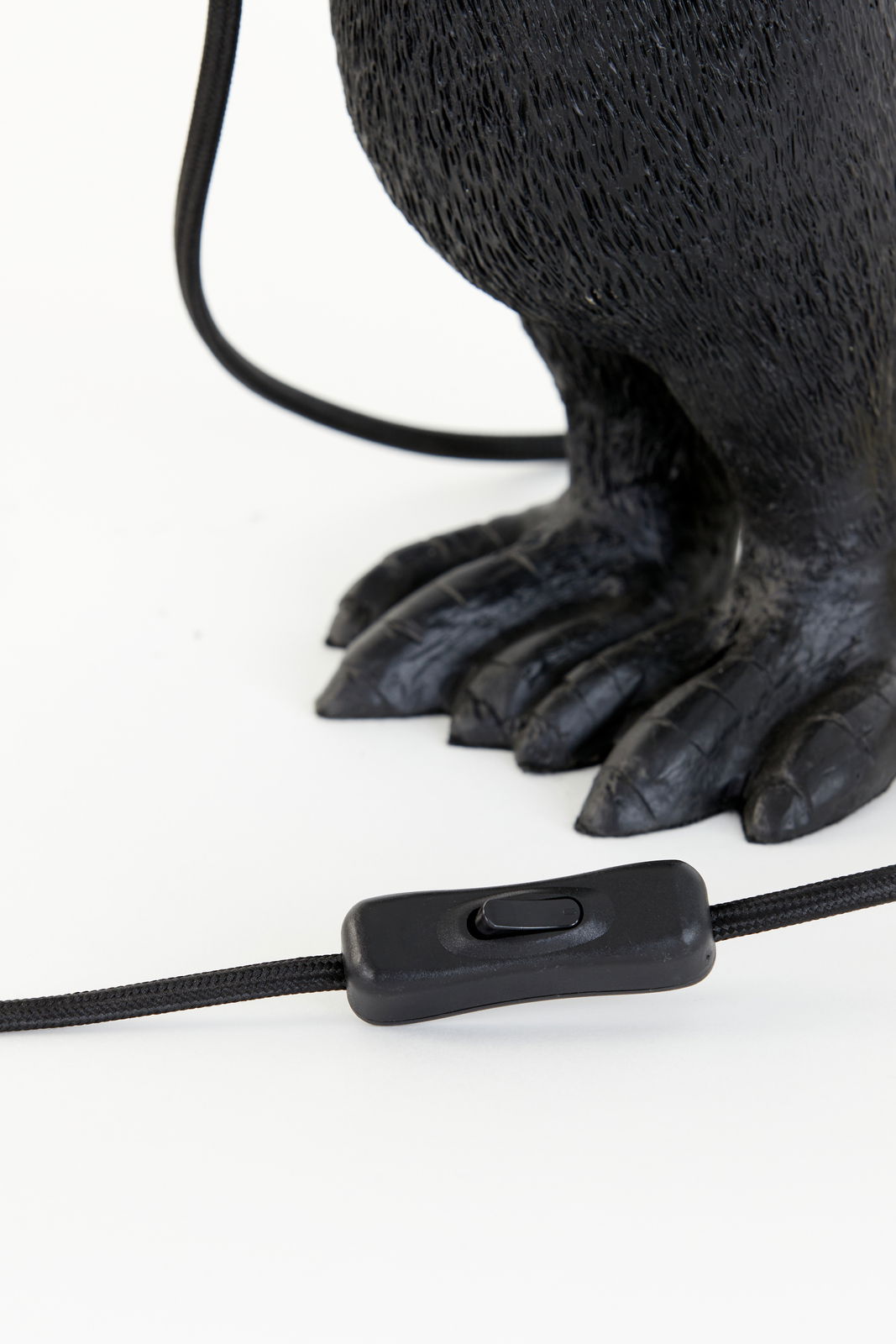 Nahaufnahme der Tischleuchte mit einem schwarzen Kabel und Schalter, sowie einem dekorativen Fuß in Tierform. Perspektive von unten.