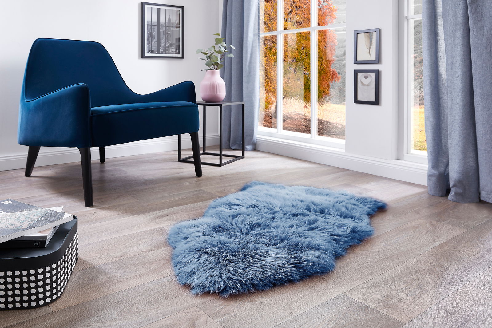 Luxor living Schaffell FELLE Blaues Schaffell auf einem Holzboden in einem modernen Wohnzimmer mit einem blauen Sessel und einem Fenster mit herbstlicher Aussicht, aus der Vogelperspektive.