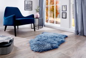 Blauw schapenvacht op een houten vloer in een moderne woonkamer met een blauwe fauteuil en een raam met een herfstachtig uitzicht, gezien vanuit vogelperspectief.