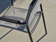 Nahaufnahme eines modernen Stapelsessels mit schwarzem Metallrahmen und grauer Seilbespannung, von oben betrachtet.