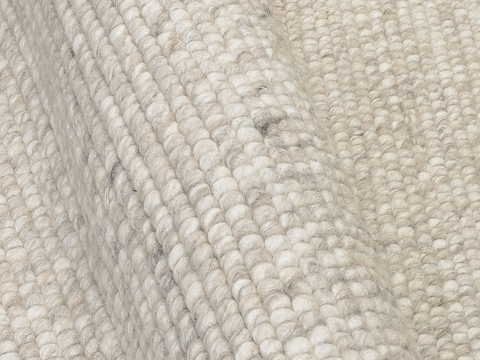 Nahaufnahme eines handgewebten Teppichs mit grober Struktur in neutralen Farbtönen, seitliche Perspektive.