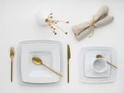 Minimalistisches Tischgedeck mit weißen quadratischen Tellern, goldfarbenem Besteck, weißer Tasse und beigefarbenen Stoffservietten mit Trockenblumen auf weißem Hintergrund, Draufsicht von oben