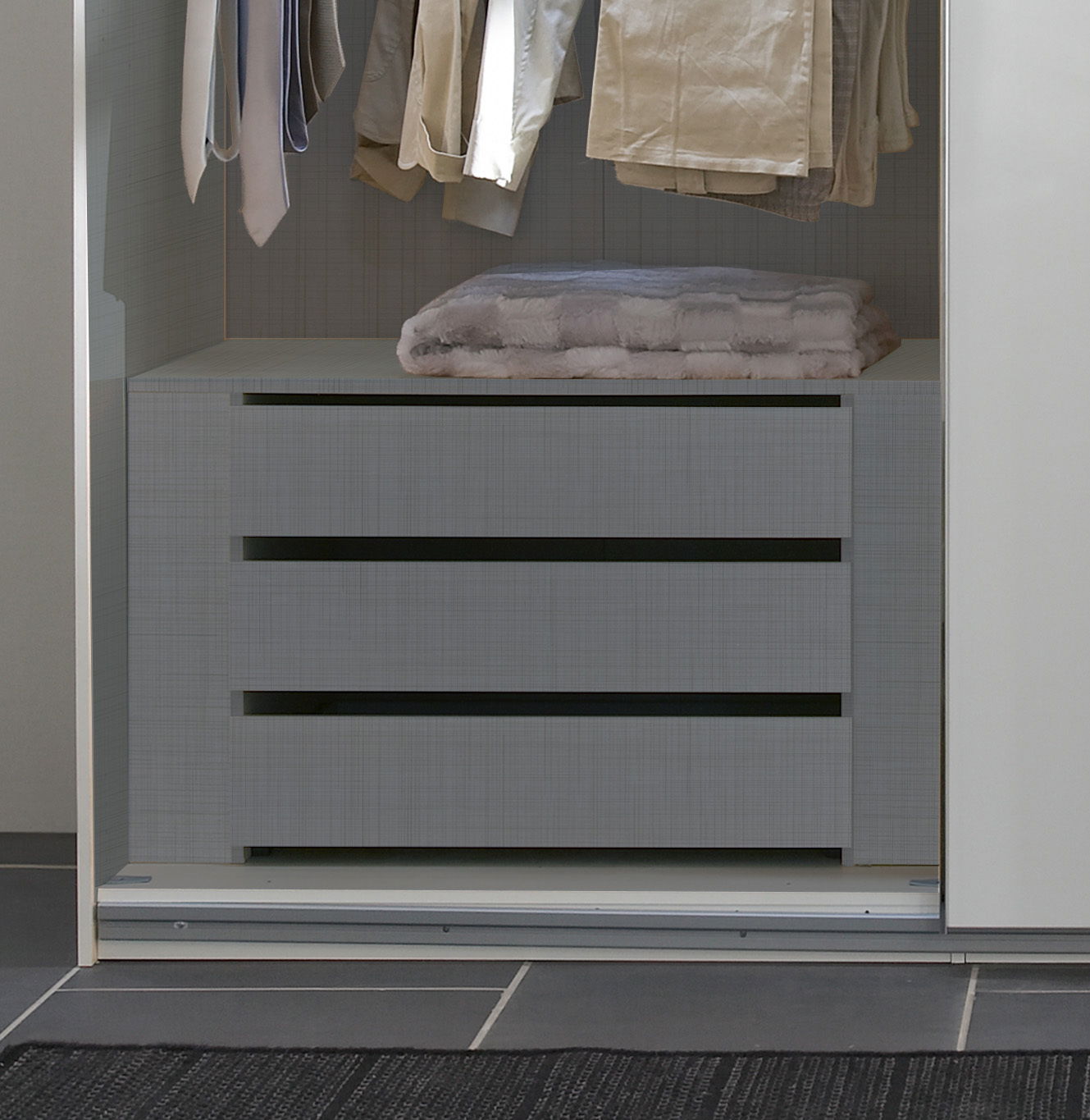 Schubkasteneinsatz in einem Kleiderschrank, frontal betrachtet, mit hängender Kleidung darüber.