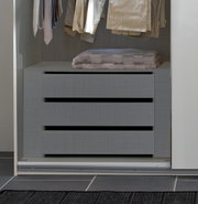 Schubkasteneinsatz in einem Kleiderschrank, frontal betrachtet, mit hängender Kleidung darüber.