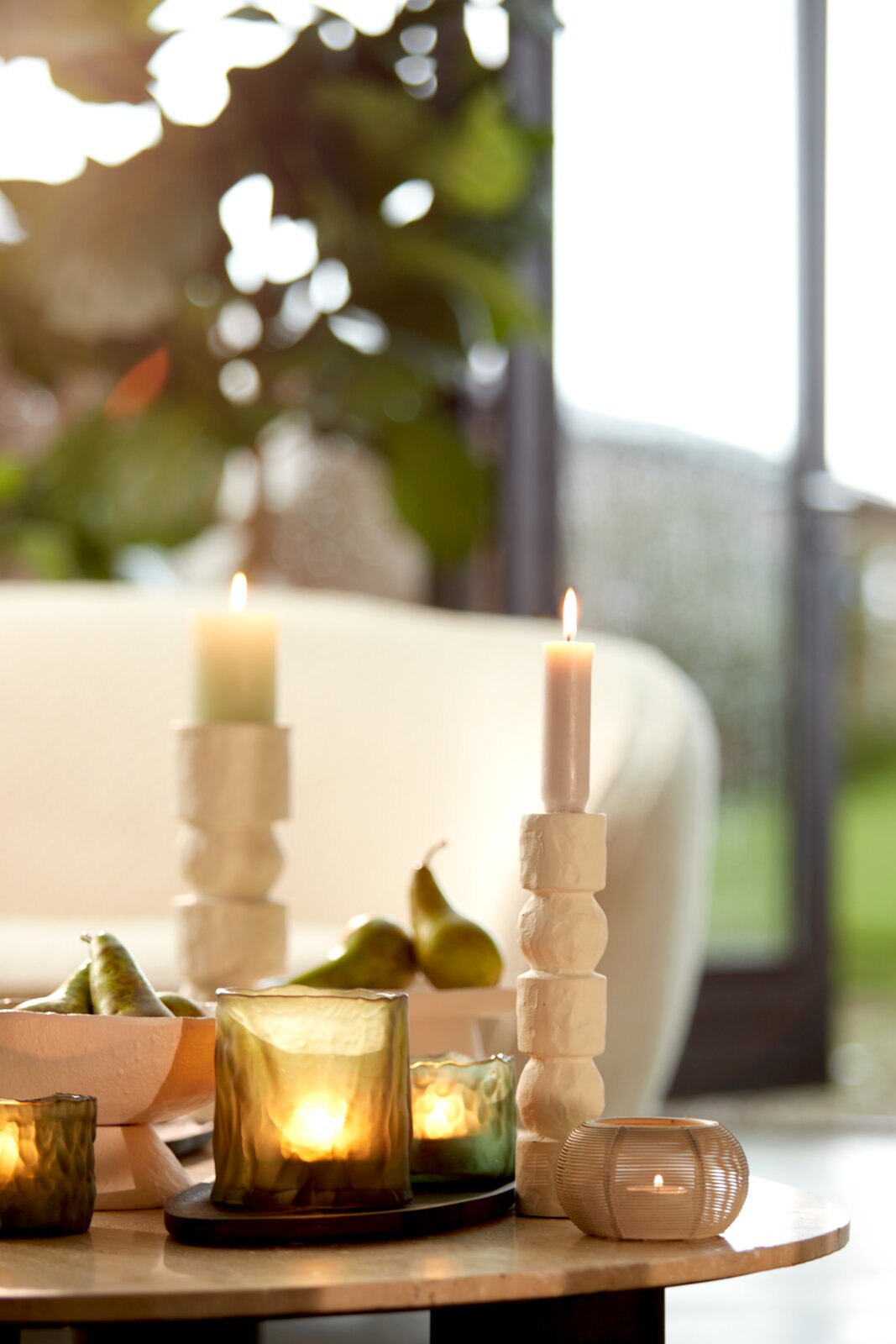Een theelichtje in een matglazen houder op een tafel, omringd door andere kaarsen en decoraties, gefotografeerd vanuit een zijdelingse hoek.