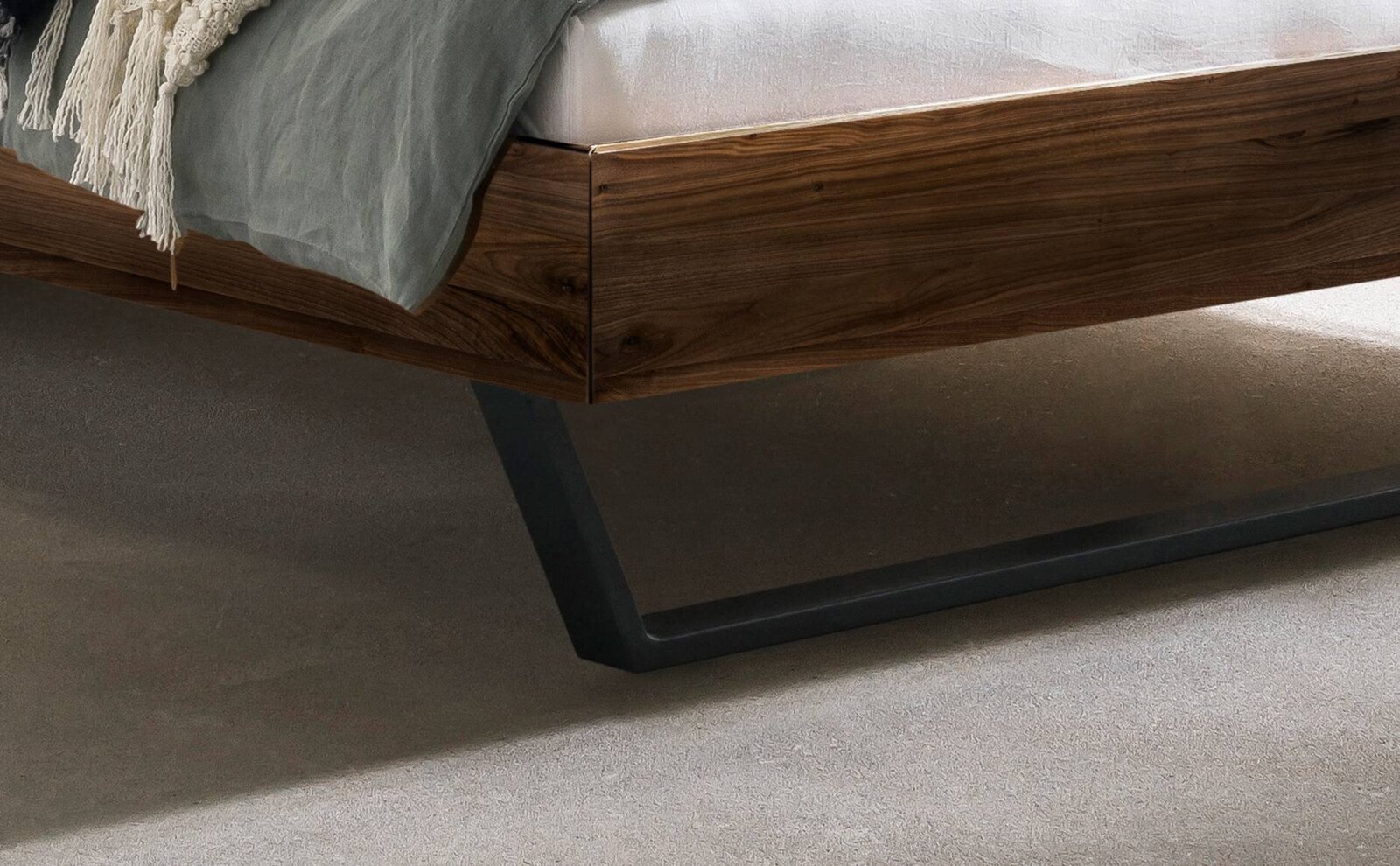 Close-up van een modern houten bedframe met metalen poten, gezien vanaf de zijkant.