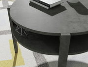 Ronde salontafel van donker materiaal met twee niveaus, gezien van bovenaf. Op het bovenste niveau liggen boeken, het onderste niveau is leeg.