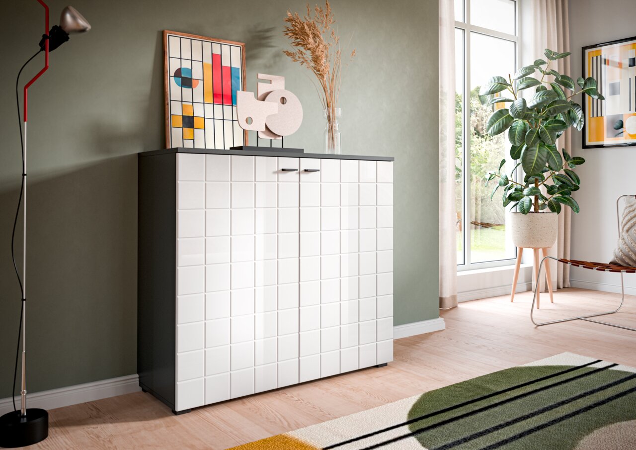MID.YOU Kommode MONTE Moderne Kommode mit weißer, quadratischer Front und dunklem Korpus, dekoriert mit Kunstobjekten und Pflanzen, in einem hellen Raum mit großen Fenstern, seitliche Perspektive.