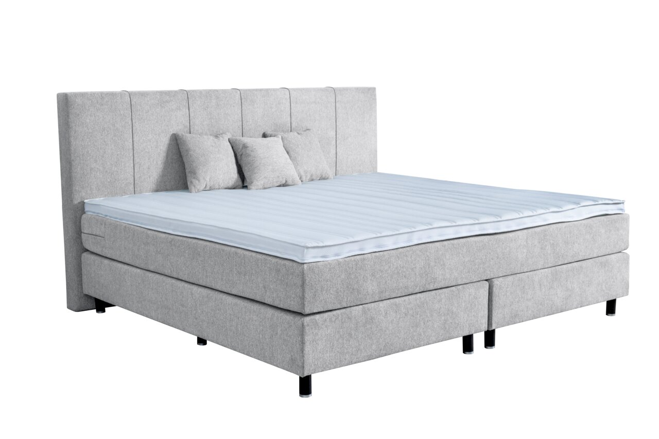 Graues Boxspringbett mit hohem Kopfteil und drei Kissen, seitliche Perspektive