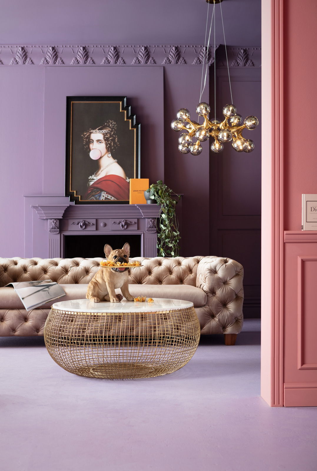 Deko-Figur eines sitzenden French Bulldog Butlers mit Tablett im Maul, auf einem runden Tisch in einem stilvoll eingerichteten Raum mit lila Wänden und einem eleganten Sofa. Perspektive: Frontalansicht.