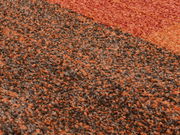 Nahaufnahme eines mehrfarbigen Teppichs mit orange-braunen Tönen, perspektivisch von oben betrachtet.