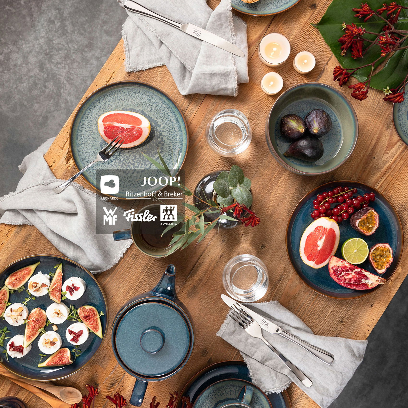 Stilvoll gedeckter Holztisch mit blauem Geschirr, Besteck, frischen Früchten, Kerzen und dekorativen Stoffservietten