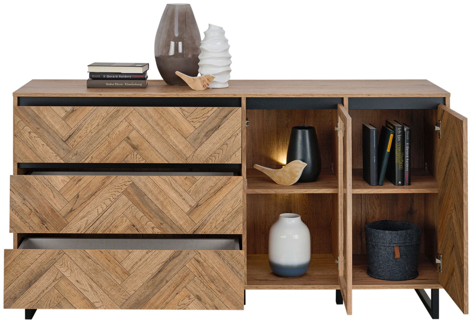 Sideboard aus Holz mit Fischgrätmuster, drei Schubladen und zwei offenen Türen, dekoriert mit Vasen, Büchern und einer Lampe, Frontalansicht.
